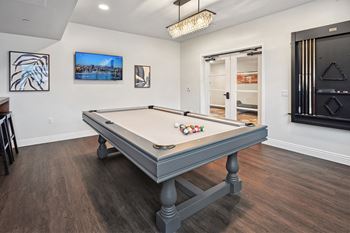 A pool table in a room with a television and picture frames on the wall.